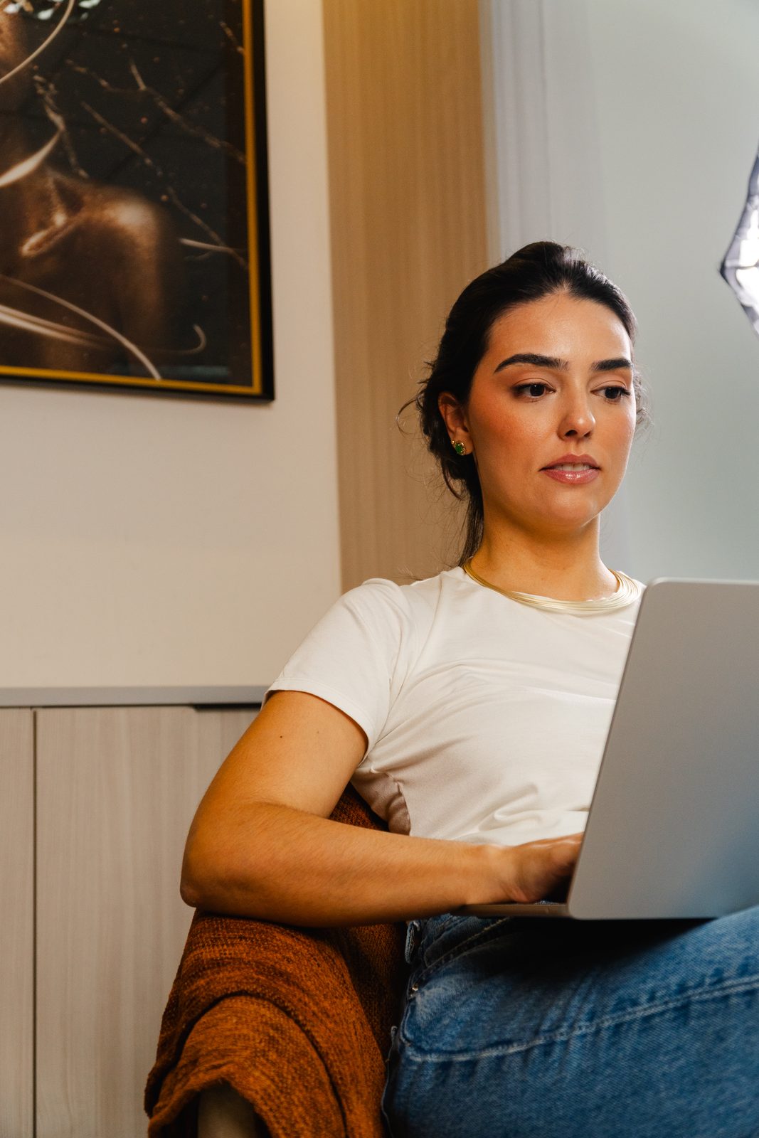 Thaís Dal Piaz sentada, de camiseta branca, lendo a tela do notebook